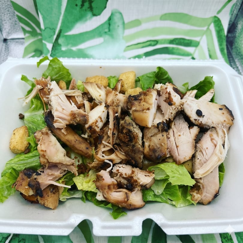 A takeout container filled with a salad of green lettuce, grilled chicken, and croutons.